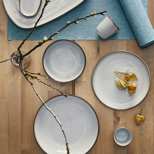 Cuenco GLADELIG con esmalte arenoso sobre mesa de madera, entre platos, diseño clásico.