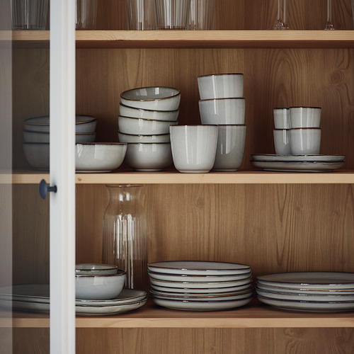 Estantes de madera con cuencos GLADELIG, blancos con esmalte gris, cuidadosamente apilados. Los cuencos varían en tamaño, los más pequeños anidados dentro de los más grandes.