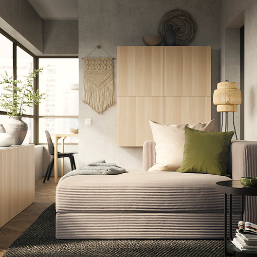 Dormitorio moderno con sofá JÄTTEBO en tonos neutros, paneles de madera y tapiz de macramé, que ofrece una estética acogedora y minimalista.