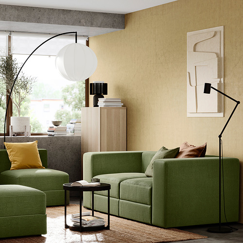 Sala de estar moderna con juego de sofás JÄTTEBO verde, cojines amarillos, lámpara de pie negra y arte de pared beige.