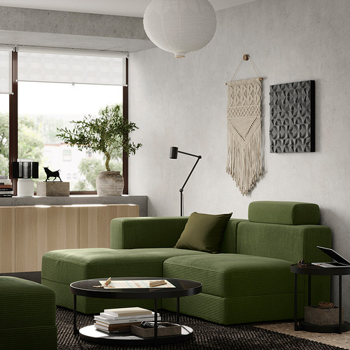 Sala de estar moderna con sofá modular verde oliva, mesa de centro negra, lámpara colgante, arte de pared y planta en maceta.