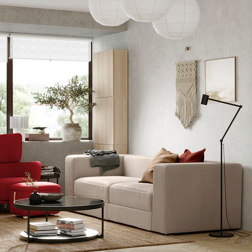 Sala de estar moderna con sofá JÄTTEBO, silla roja, lámpara, mesa de café, libros y ventana con vista al olivo.