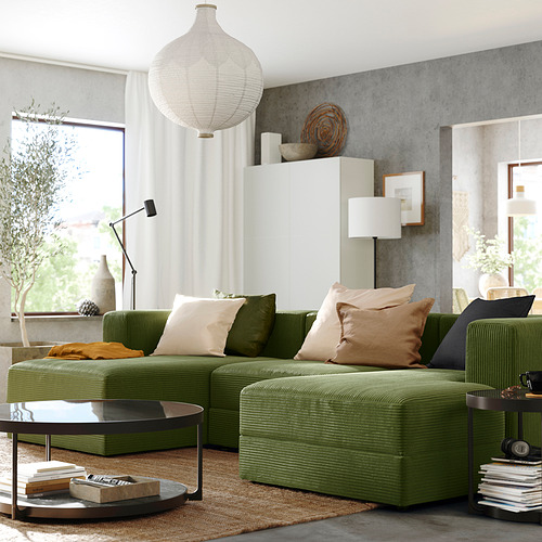 Moderno salón con sofá modular JÄTTEBO verde, grandes cojines, mesa de centro redonda, lámpara colgante y gran ventanal con cortinas blancas.