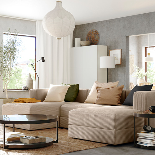 Sala de estar moderna con sofá modular JÄTTEBO beige, cojines, mesa de centro redonda, lámpara y alfombra bajo una gran ventana.