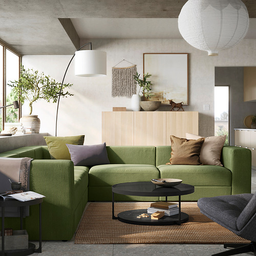 Luminoso salón con sofá JÄTTEBO de pana verde, mueble de madera natural, grandes plantas, alfombra texturizada, lámparas colgantes y decoración moderna.
