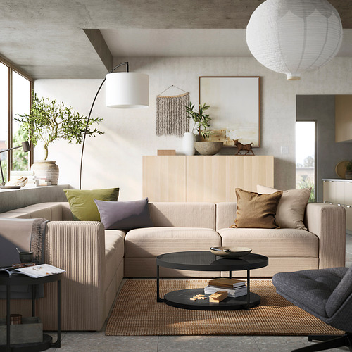 Sala de estar moderna, un sofá modular JÄTTEBO de color beige claro con almohadas de colores, un gabinete de madera con decoración y una mesa de centro negra sobre una alfombra tejida.