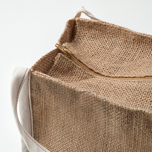 Primer plano de una bolsa de yute tejida duradera con asas de algodón, con un tirador de cremallera dorado.