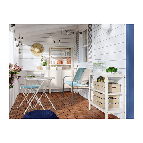 Balcón luminoso con suelo de madera, muebles blancos, cojines azules, plantas y guirnalda de luces.
