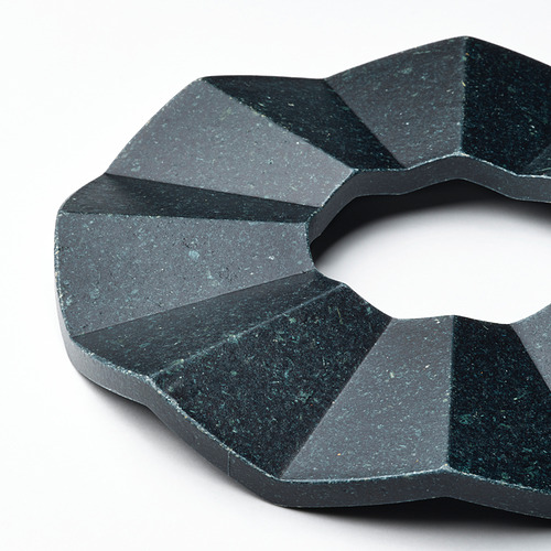 Soporte circular de textura oscura con diseño geométrico, hecho de bambú comprimido, que protege las superficies y agrega una decoración moderna.