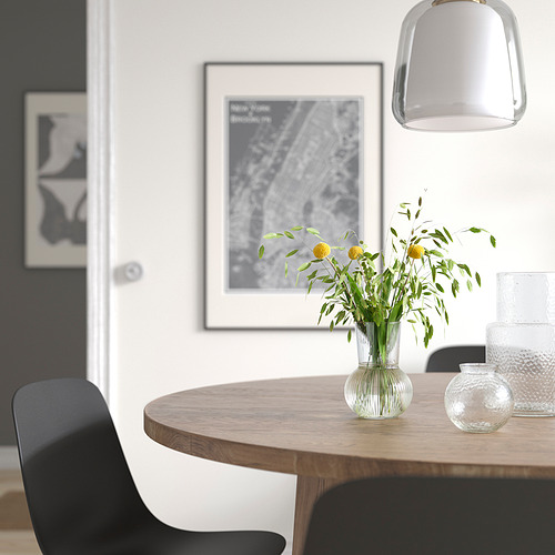 Comedor moderno con mesa redonda, sillas negras, flores amarillas en jarrón de vidrio, lámpara colgante, arte en la pared.