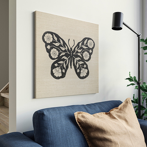 Lienzo beige con mariposa negra sobre sofá azul, lámpara parcial.