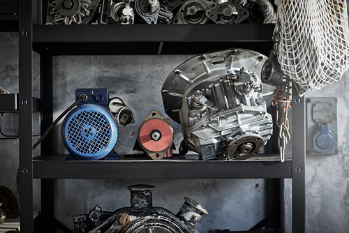 Estante de metal negro con varias piezas industriales, incluidos engranajes, un motor azul y componentes metálicos.
