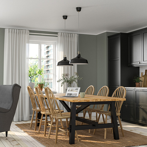 Cocina moderna Juego de comedor SKOGSTA con mesa de madera con detalles en negro y sillas con respaldo de huso cerca de una gran ventana, rodeada de gabinetes oscuros.