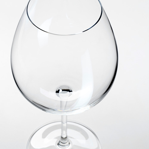 Una copa de vino clara y vacía con un tallo largo y un recipiente ancho, que refleja la luz, sobre un fondo blanco.