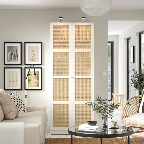 Sala de estar moderna con estanterías blancas BILLY, con puertas de bambú, un sofá blanco, una mesa de centro de vidrio y una decoración natural.