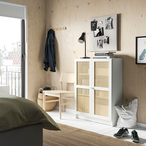 Dormitorio moderno con pared de madera clara, armario blanco, abrigo negro y manta verde.