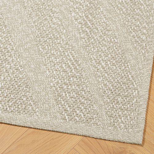 Alfombra tejida de color beige de alta calidad sobre suelo de madera, que muestra una textura y artesanía intrincadas.