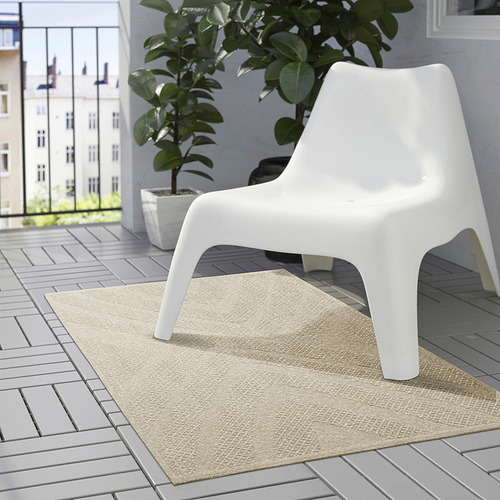 Patio moderno con alfombra beige, silla blanca y gran planta verde.