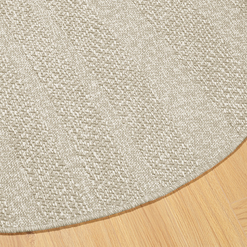 Alfombra redonda con estampado beige texturizado sobre suelo de madera, que muestra su intrincado tejido y sus bordes suaves.