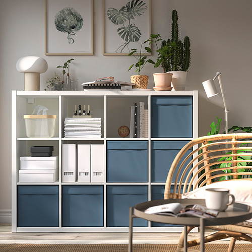 Sala de estar moderna con almacenamiento azul, libros, plantas y decoración. Silla de mimbre con cojines verdes en primer plano.