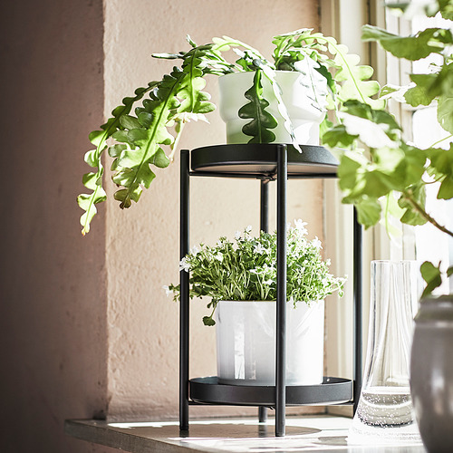 Las plantas OLIVBLAD negras se colocan en varios niveles, mostrando plantas verdes en macetas blancas. Diseño moderno para uso en interiores o exteriores.