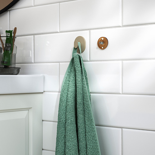 Toalla verde colgada en gancho adhesivo de pared en el baño.