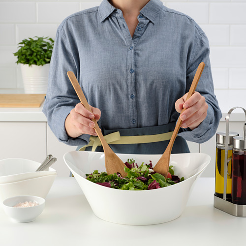 Persona echando ensalada en un tazón con ingredientes de cocina.