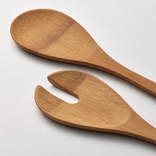 Cuchara y tenedor de madera, pulidos y lisos, que descansan sobre una superficie gris.