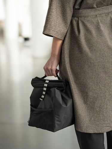 Persona sosteniendo un bolso FRAMTUNG negro, asa redonda, abrigo gris a cuadros.
