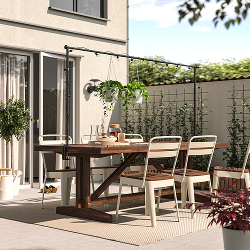 Comedor al aire libre con mesa de acacia, sillas de metal, plantas y luces. Perfecto para patios.
