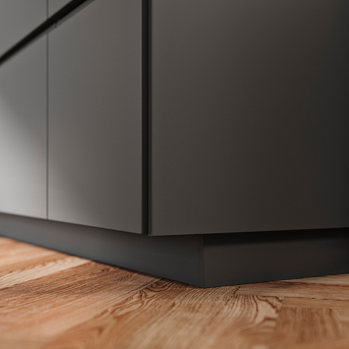 Un zócalo de armario de cocina FÖRBÄTTRA gris hecho de lámina de plástico y polipropileno, perfectamente encajado contra un suelo de madera.