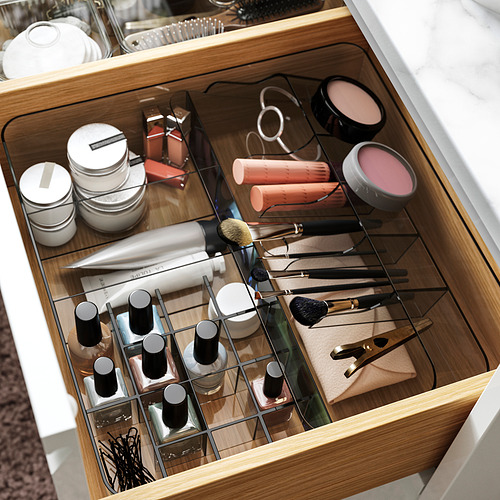 Organizador de cajones de plástico transparente con múltiples compartimentos para artículos pequeños como brochas de maquillaje, tubos y contenedores.