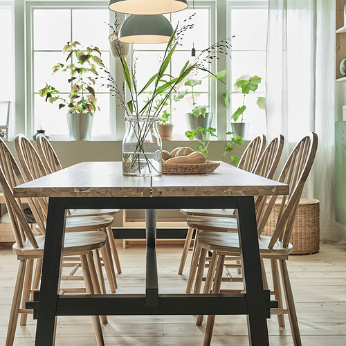 Juego de comedor SKOGSTA: mesa de acacia, base de metal negro, sillas a juego y jarrón de plantas secas.