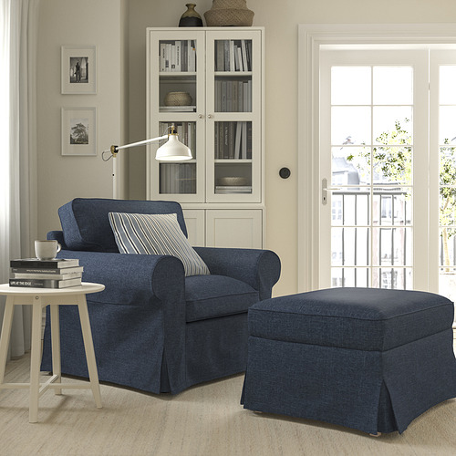 Sillón y otomana azul marino EKTORP, acogedor y de gran tamaño, con mesa auxiliar blanca y estantería de cristal.