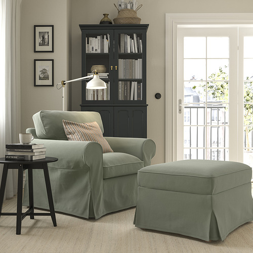 Acogedora sala de estar con sillón EKTORP verde, reposapiés, mesa auxiliar y estantería. Luz natural a través de un gran ventanal.