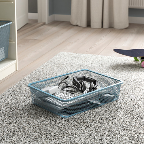 Caja de almacenamiento de malla sobre alfombra, con auriculares y cargador, parte del sistema TROFAST.