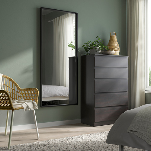 Espejo grande NISSEDAL, marco negro, colocado verticalmente, junto a la cajonera gris en el dormitorio. La superficie reflectante muestra la cama.