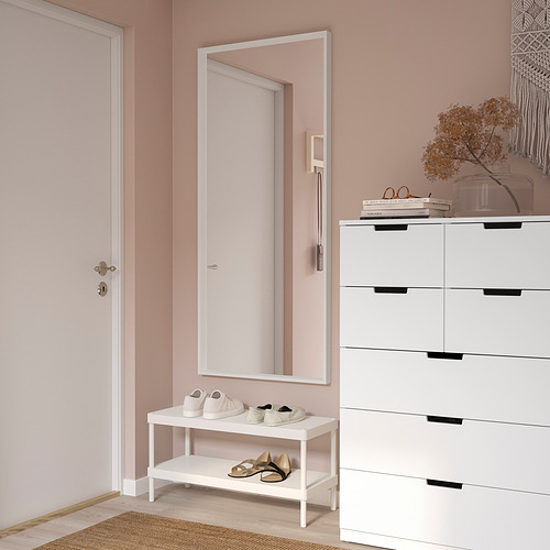 Un espejo de pared rectangular blanco NISSEDAL, más grande que el zapatero y la cómoda que había a su lado, colgaba verticalmente de una pared rosa en un pasillo.