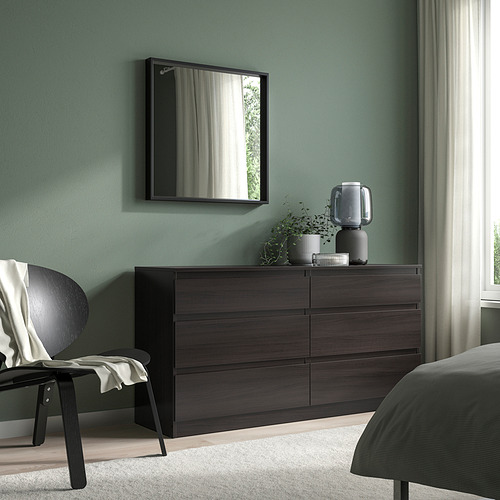 Dormitorio moderno con espejo NISSEDAL, cofre, plantas, lámpara, silla y manta contra paredes de salvia.
