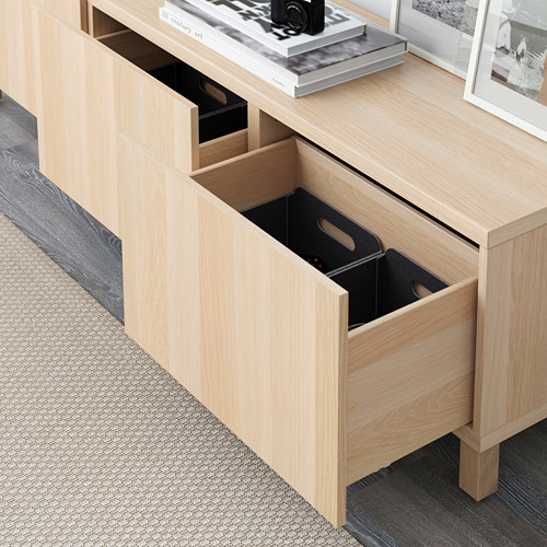 Cajonera de madera clara con tres cajones abiertos, dejando ver cajas negras en su interior. Mecanismo de cierre suave visible. Forma parte del sistema de almacenamiento BESTÅ.