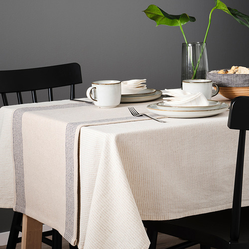 Mesa preparada con mantel SILVERARV, tazas, platos y cubiertos blancos en sillas oscuras.