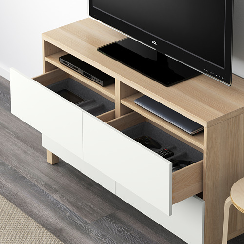 Moderno mueble de TV con cajón abierto que muestra el control remoto y los cables, que alberga un televisor de pantalla plana y dispositivos electrónicos.