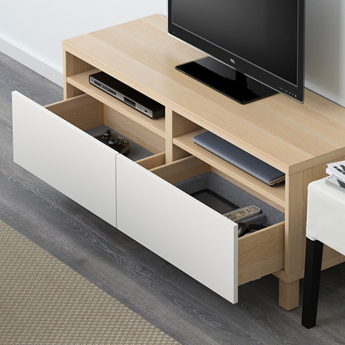 Mueble de TV de madera con cajón extraído que sostiene los controladores de juegos y el control remoto. Televisor de pantalla plana en la parte superior, con dispositivos de entretenimiento visibles.