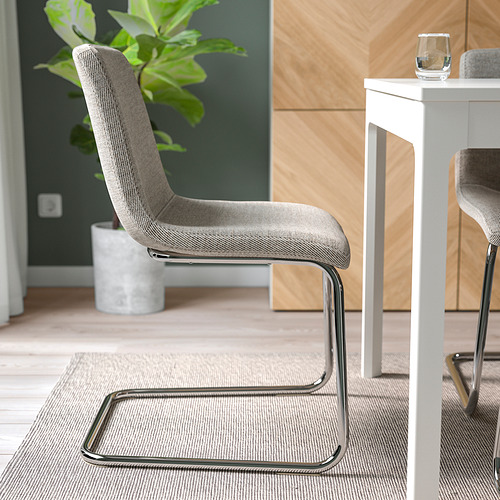 Dos modernas sillas tapizadas alrededor de una mesa de comedor con un vaso. Las sillas tienen un diseño en voladizo para mayor comodidad y flexibilidad.
