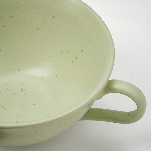 Taza vidriada verde con motas, asa sólida, superficie blanca.