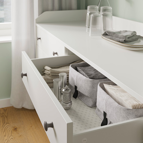 Cajón HAUGA blanco abierto con contenedores de almacenamiento organizados de color gris claro y ropa de cama doblada. Mangos negros.