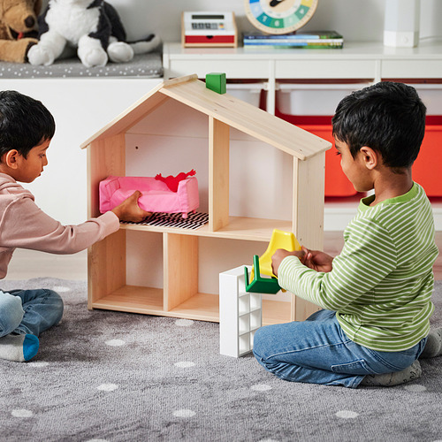 Niños jugando con la casa de muñecas FLISAT; uno agrega sofá, otro sostiene bloques. Doble juguete y estantería.
