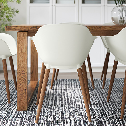 Moderno juego de comedor con sillas blancas y mesa de madera sobre una alfombra estampada. Fácil de limpiar y duradero.
