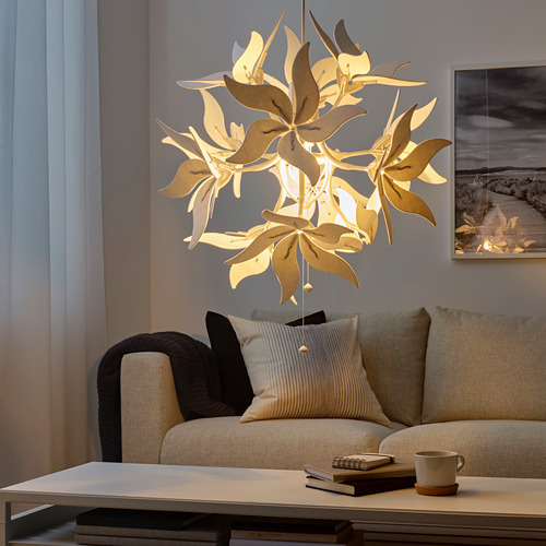 Colgante floral único de luz, sala de estar moderna con sofá beige, mesa de centro y libros. Ilumina numerosos tonos en forma de hojas, proyectando una iluminación cálida.