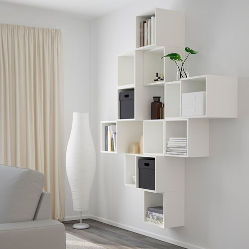 Modern living room featuring EKET storage with books, vases, and plants. Beige curtains and gray sofa.